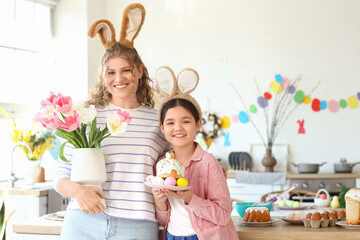 Happy mother with her daughter holding Easter cake and tulips in kitchen