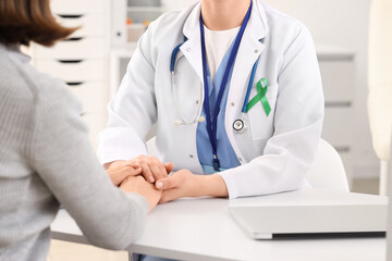 Female doctor with pink ribbon and patient holding hands in clinic, closeup. Breast cancer...