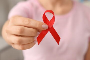 Young woman with red ribbon in clinic, closeup. Blood cancer awareness concept