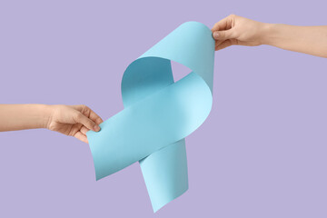 Female hands with blue ribbon on lilac background. Cancer awareness concept