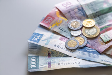 Close-up macro of Mexican pesos of different denominations in the form of a fan with coins on top against a white background