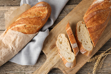 Fresh baguettes and spikes on wooden table, flat lay