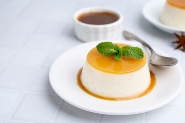 Tasty pudding with caramel sauce served on white tiled table, closeup. Space for text