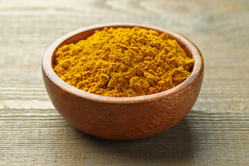 Turmeric powder in bowl on wooden table, closeup