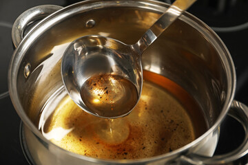 Pouring used cooking oil from ladle into saucepan, closeup