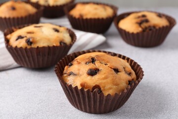 Delicious muffin with chocolate chips on light grey table, closeup