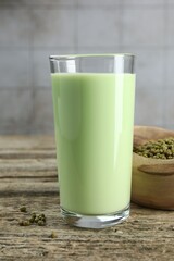Fresh mung bean juice in glass and seeds on wooden table against grey wall, closeup