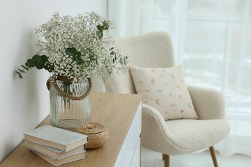Beautiful gypsophila flowers with eucalyptus branches in vase and books on commode at home. Space...