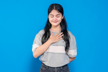 Young Asian woman with a warm smile, placing one hand on her chest, expressing gratitude and...
