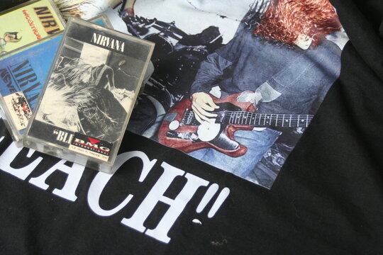 A collection of iconic Nirvana cassette tapes, including "Incesticide," "Bleach," and "Nevermind," artistically arranged on a black Nirvana T-shirt, perfect for music enthusiasts and collectors.