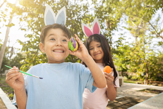 Happy kids painting easter eggs outdoors with bunny ears - Creativity and Fun in Spring