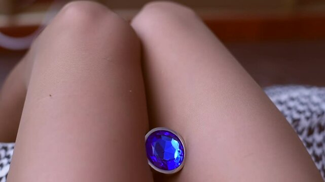 Metal anal plug with blue cristal spinning between on a beautiful female legs in nylon tights.