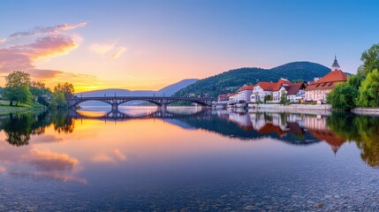 Fototapeta premium A tranquil riverside scene at sunset, featuring a picturesque bridge, charming houses, and reflecting mountains in the water.