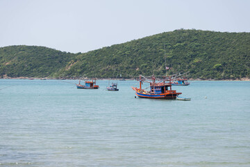 Fototapeta premium Experience the tranquility of serene waters adorned with vibrant fishing boats and lush green hills, reflecting the beauty of natures coastal landscape in perfect harmony.
