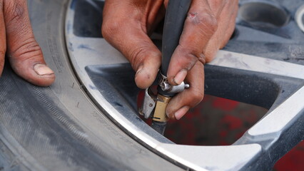 A mechanic staff hand is filling the air for the car tires. 