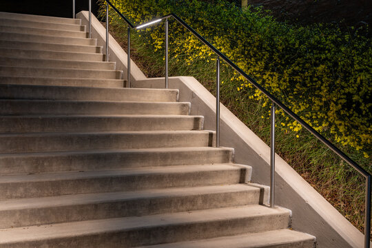 Exterior night photo of a set of concrete stairs with stainless steel railing with integrated under rail LED lighting. - Powered by Adobe