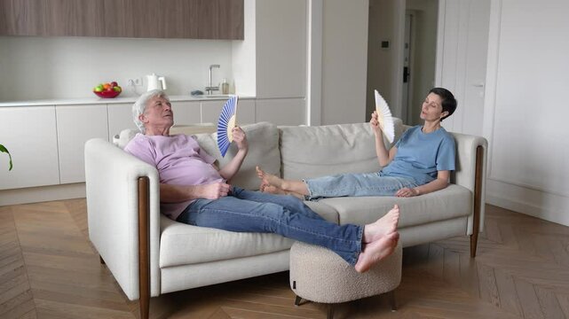 Fatigued tired family fanning on sofa, unable to do anything. No air conditioning, sweltering indoors, hard to breathe, suffocating, heat exhaustion, overwhelm discomfort and increased blood pressure