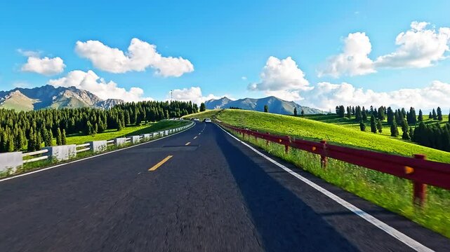 Asphalt road through vibrant green hills towards mountains under blue sky