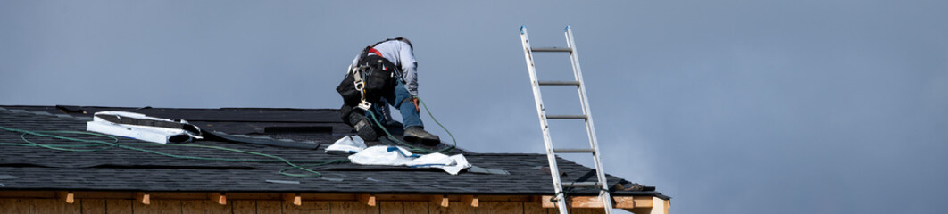 New home construction site, roofing contractor (workman labor) putting down asphalt shingles, housing development on a sunny winter day against a stormy sky  © knelson20
