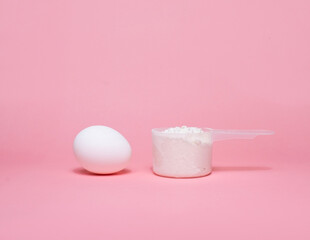 A scoop of dietary supplements and an egg on a soft pink background, highlighting nutrition, protein, and healthy eating for fitness enthusiasts.