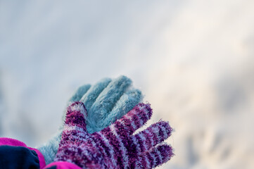 A pair of mismatched gloves on a child held over a white snow background
