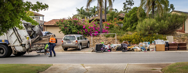 A large garbage truck collecting large bulky waste items from a suburban street.