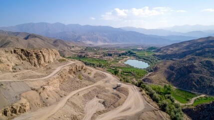 High-angle view of a valley with winding roads, a small lake, and mountains in the background