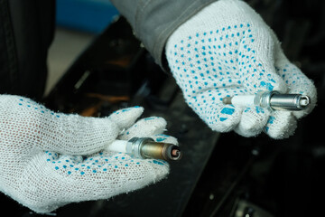Auto parts. An auto mechanic demonstrates a faulty spark plug and prepares the installation of a...