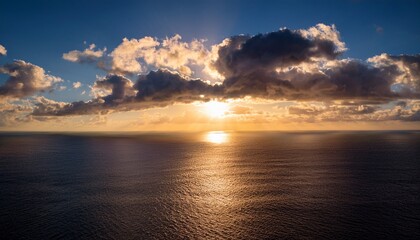 Fototapeta premium a sun drenched sky over a tranquil sea with fluffy clouds casting shadows on the rippling surface reflecting the golden light in a shimmering dance