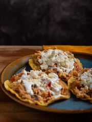 Tostadas with chicken tinga, cheese and cream on a plate on a wooden table. Typical Mexican food