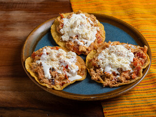 Tostadas with chicken tinga, cheese and cream on a plate on a wooden table. Typical Mexican food