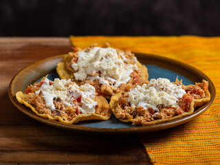 Tostadas with chicken tinga, cheese and cream on a plate on a wooden table. Typical Mexican food