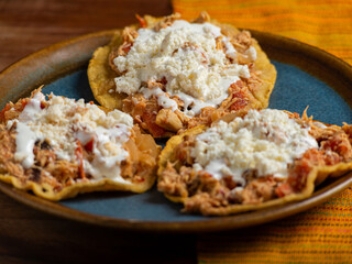 Tostadas with chicken tinga, cheese and cream on a plate on a wooden table. Typical Mexican food