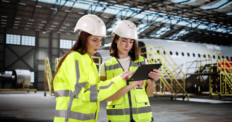 Woman with tablet checks aircraft engine at airport maintenance hangar