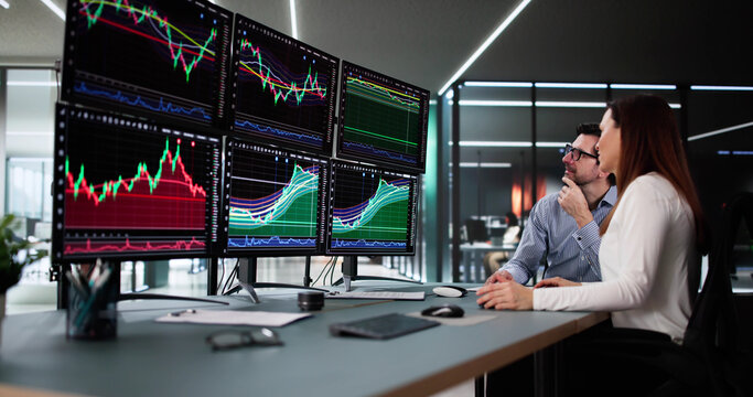 Stock trader analyzing market data on multiple monitors with financial graphs