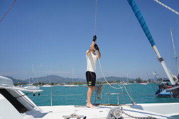 Naklejka premium Male captain on deck of sailboat opening sails pulling the rope