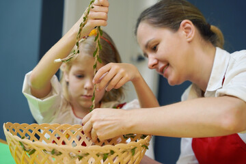 Mother and daughter at the table in traditional Ukrainian costumes weaving a basket for Easter