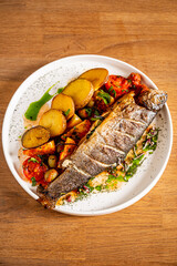 A beautifully arranged dish of grilled fish with crisp potatoes and vibrant vegetables