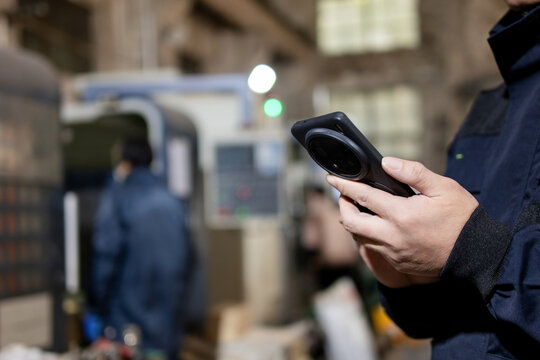 Asian male blue  collar workers are using smart phone in a metal processing factory