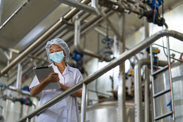 Female inspector wearing protective gear and hairnet examines canned fish production quality, checks Industrial pressure cooker, monitors food processing , and records data using tablet.