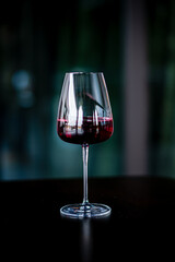 A glass of red wine rests on a dark table, reflecting light and inviting relaxation