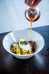 A cozy moment reveals a hand drizzling flavorful broth over delicate tortellini with rich mushrooms