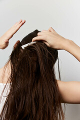 Fototapeta premium hair care, hairstyle, grooming, beauty, personal care A woman with long, wet hair is styling her hair using a hair comb against a neutral light background, emphasizing self care and personal grooming