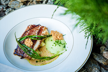 Delightful grilled fish plated with colorful sauces and garnishes, surrounded by natural greenery