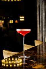 Bright red cocktail with a frothy top rests on a glimmering marble table amid an upscale bar