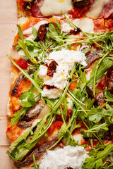 A delightful pizza featuring arugula and sun-dried tomatoes, prepared on a wooden board