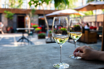 Two glasses of wine sit on a rustic table while friends chat in a lively courtyard
