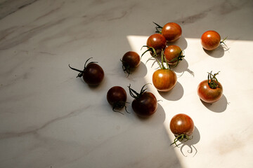 Freshly picked cherry tomatoes rest warmly in sunlight on a smooth marble countertop