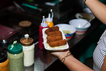 Close-up of a hand holding a styrofoam plate of fried croquettes