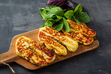 Grilled halloumi cheese sits on a wooden board with fresh herbs, inviting and tasty
